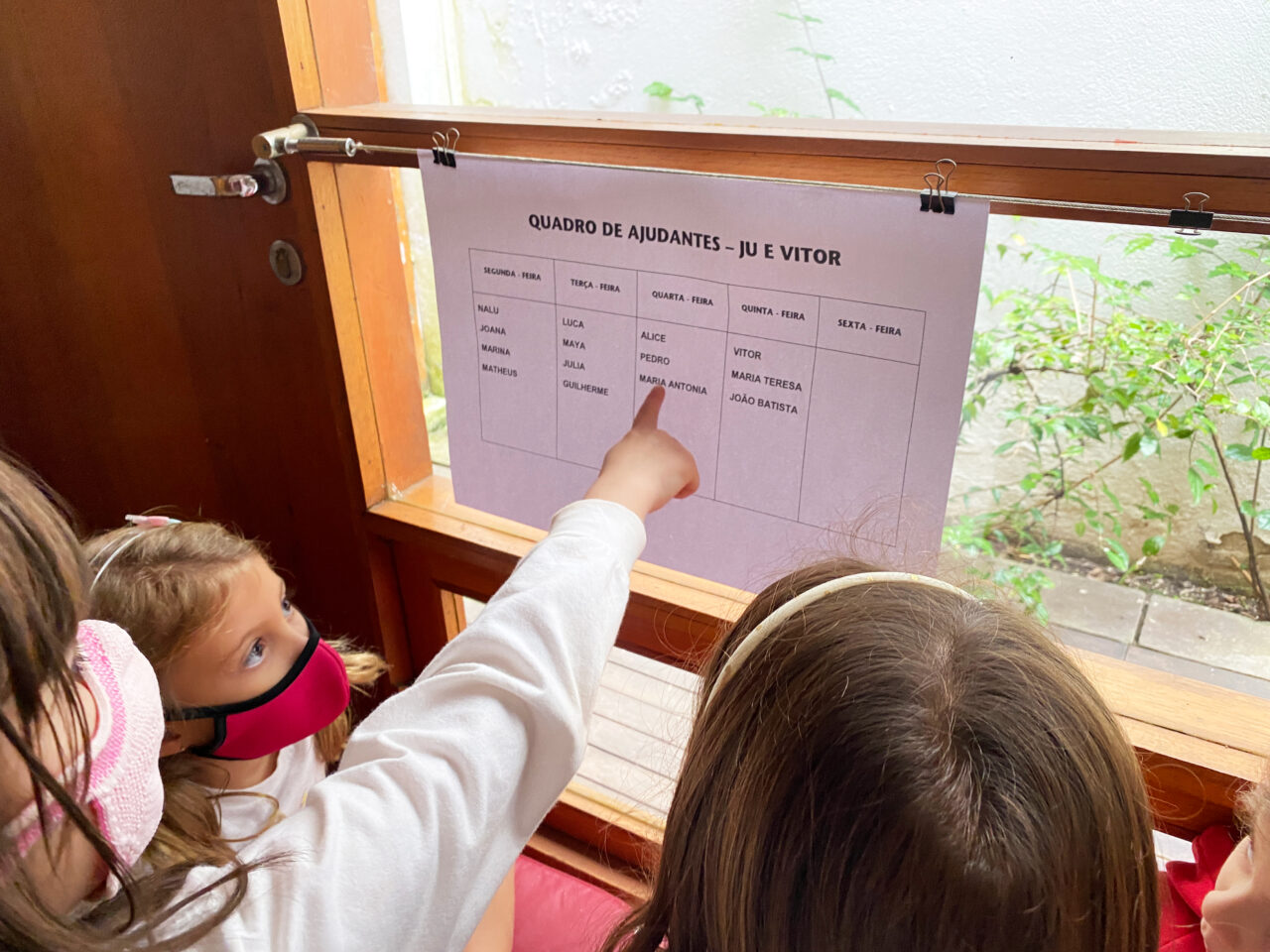 Crianças em processo de alfabetização olhando para quadro de ajudantes em sala de aula<br />
